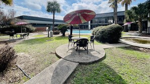 An outdoor patio area with a pool, palm trees, and a building in the background. - Extended Stay SA (San Antonio)