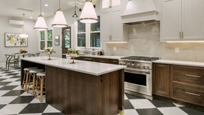 A modern kitchen with a large island, dark wood cabinets, white countertops, and pendant lighting.