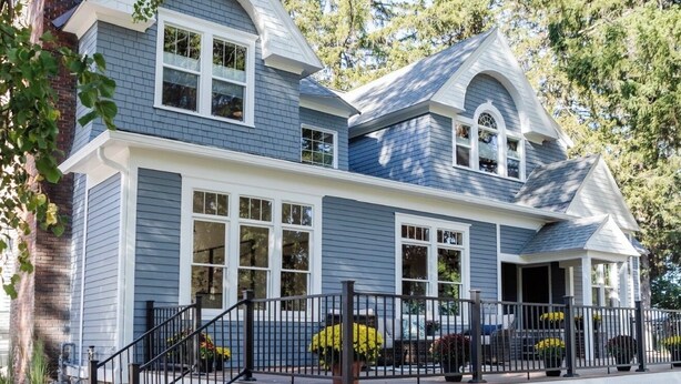 A two-story house with a covered porch, a brick chimney, and a landscaped garden.