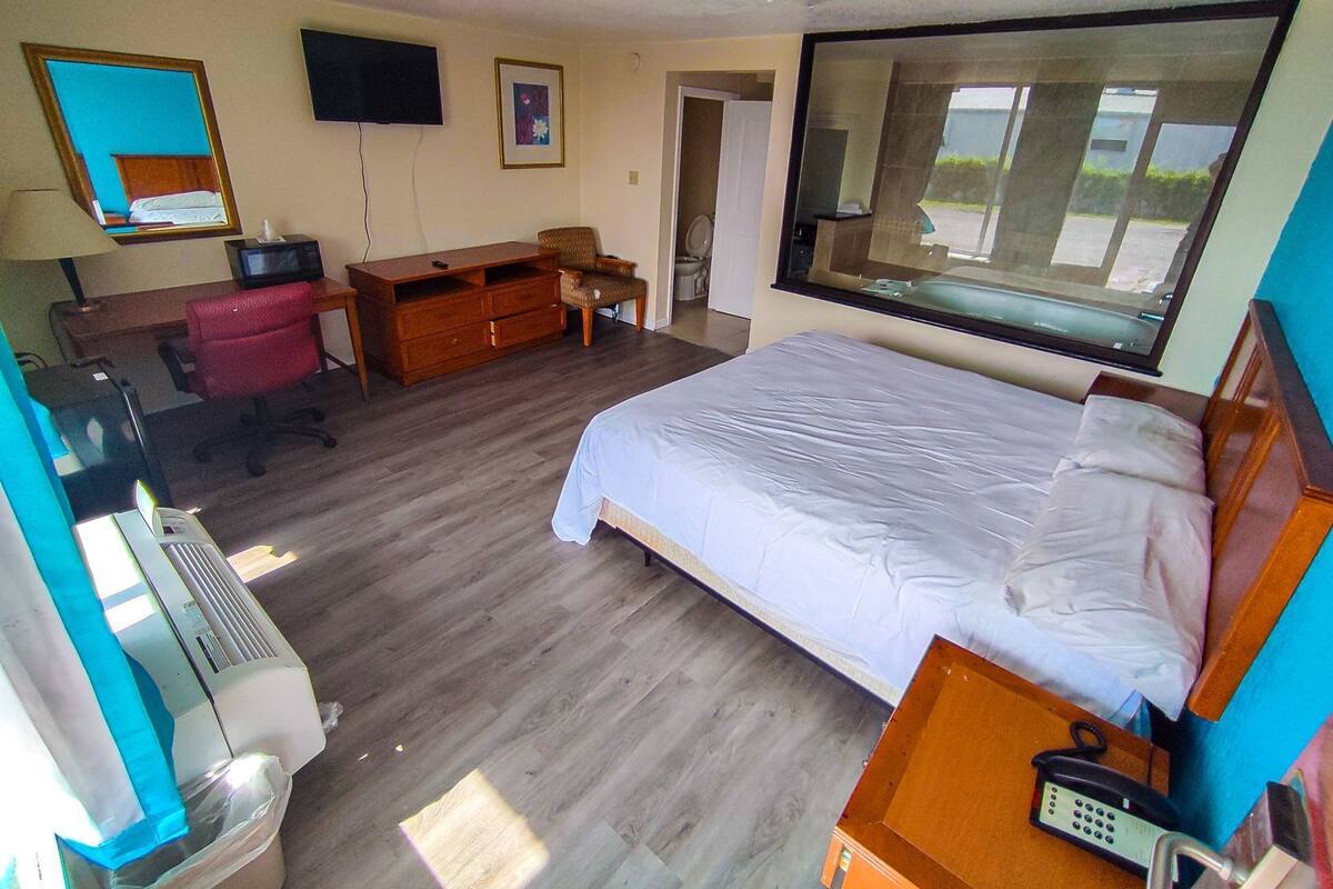 A hotel room with a bed, desk, chair, television, and a large window.