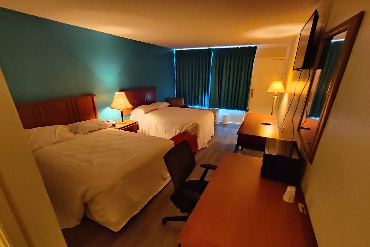 A hotel room with two beds, a desk, and a chair.