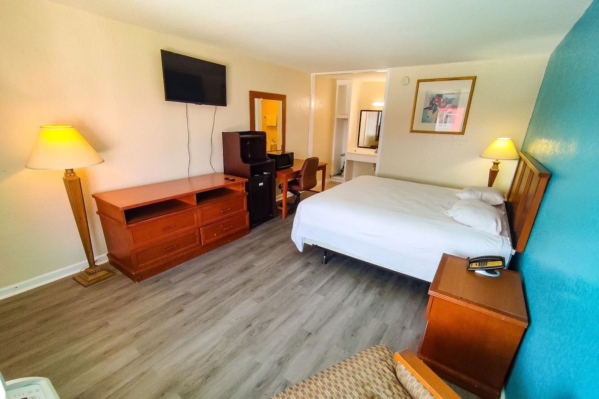 A hotel room with a bed, desk, chair, TV, and bedside table.