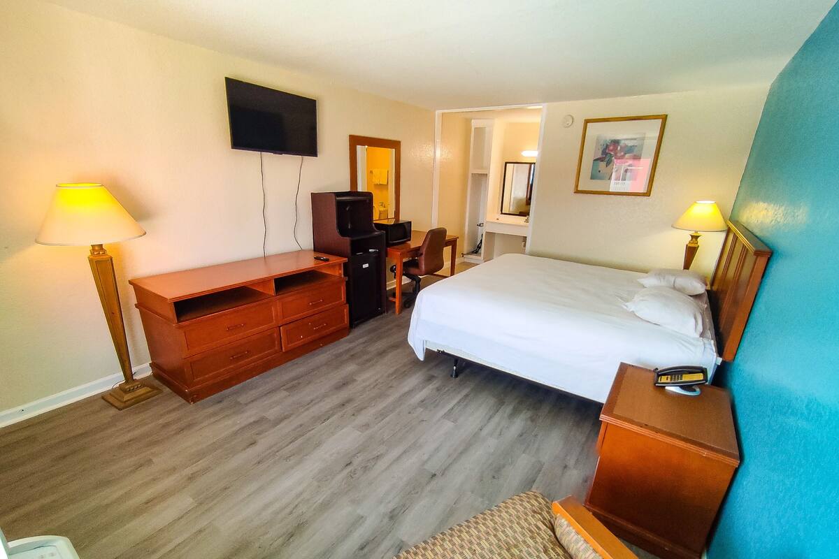 A hotel room with a bed, a desk, a chair, a TV, and a lamp.