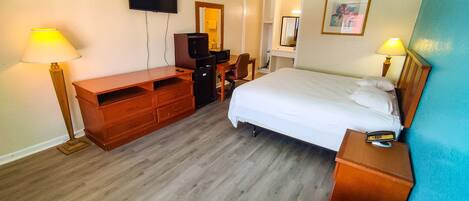 Una habitación de hotel con cama, escritorio, silla, televisor y lámpara.