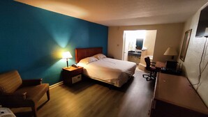 A hotel room with a bed, bedside table with a lamp, a chair, a desk with a lamp, and a mirror. - Clover Inn & Suites (Shreveport)