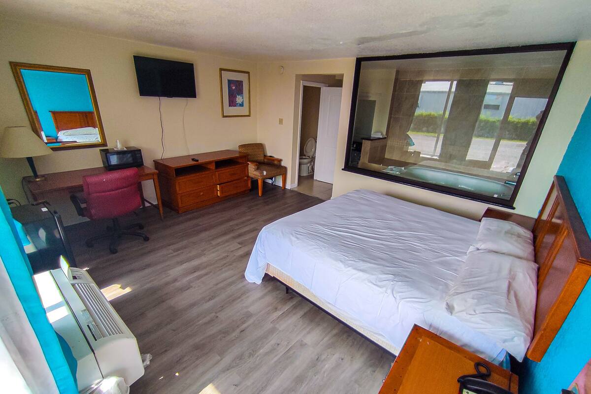 A hotel room with a bed, a desk with a computer, a chair, a TV, and a window.