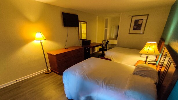 A hotel room with a large bed, a desk, a chair, a dresser, a TV mounted on the wall, and a bedside lamp. - Clover Inn & Suites (Shreveport)