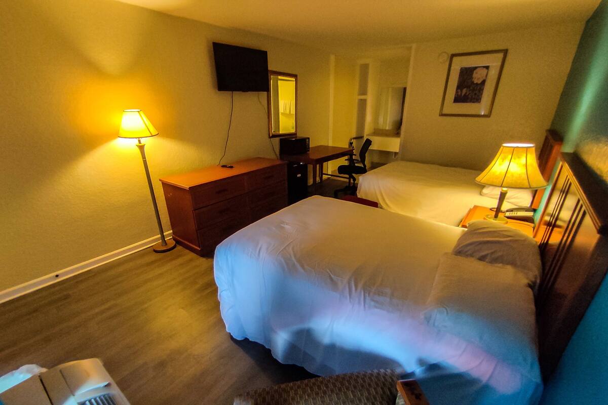 A hotel room with a large bed, a desk, a chair, a dresser, a TV mounted on the wall, and a bedside lamp.