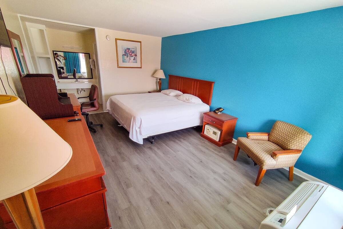 A hotel room with a bed, a desk, a chair, a nightstand, and a wall-mounted radio.