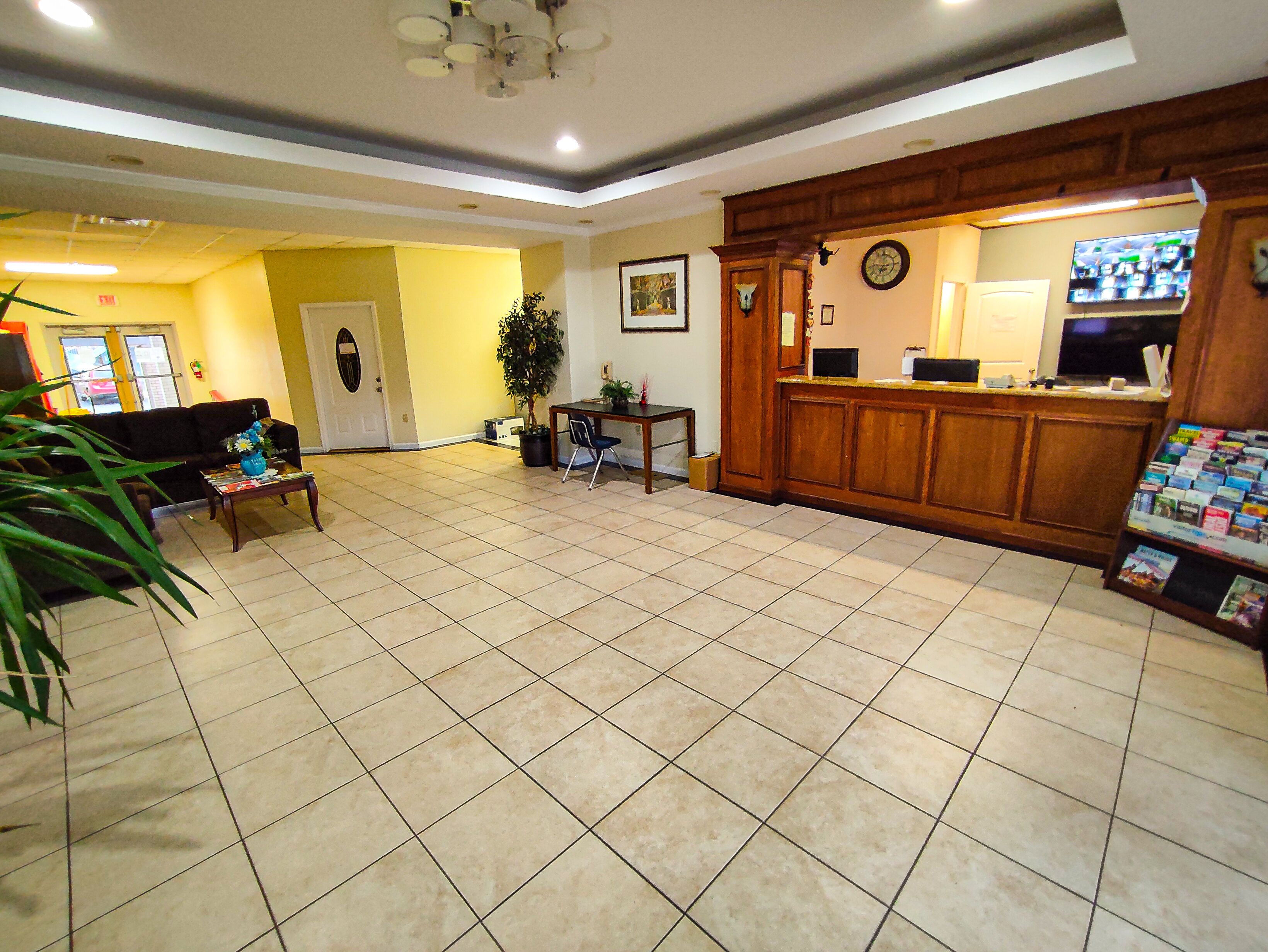 A hotel lobby with a reception desk, a seating area with a sofa and armchairs, a potted plant, and a tiled floor.