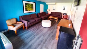 A living room with a blue wall, two sofas, a coffee table, a TV, and a small table with a lamp. - Clover Inn & Suites (Shreveport)