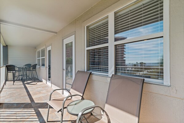 A covered patio area with a seating arrangement and large windows with blinds.