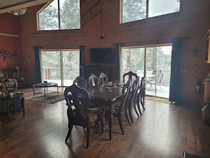 A spacious room with a large dining table surrounded by chairs, a fireplace, and large windows offering a view of trees. - Secluded Cabin in the Beautiful Black Hills! Admire the Breathtaking Scenery!  (Lead)