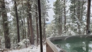 Un jacuzzi con revestimiento de madera, rodeado por un bosque nevado.