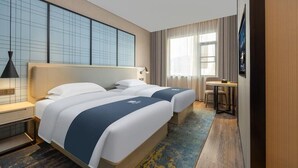 Hotelkamer met twee bedden, een bureau, een stoel, een raam met gordijnen en een wand met een rasterpatroon.