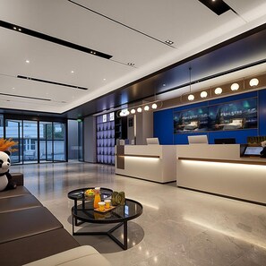 Een moderne hotellobby met een receptiebalie, een zithoek en een groot raam met uitzicht op de stad.