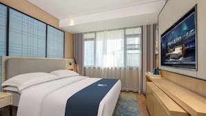 Een hotelkamer met een groot bed, een aan de muur bevestigde televisie en een bureau met een stoel.