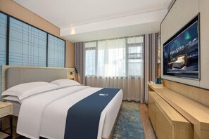 Een hotelkamer met een groot bed, een aan de muur bevestigde televisie en een bureau met een stoel.