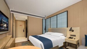 Een hotelkamer met een bed, nachtkastje, televisie en een bureau met stoel.