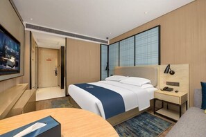 Een hotelkamer met een bed, nachtkastje, televisie en een bureau met stoel.