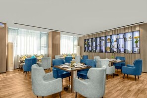 Een moderne eetruimte met blauwe fauteuils, houten tafels en een decoratieve wand met planken.