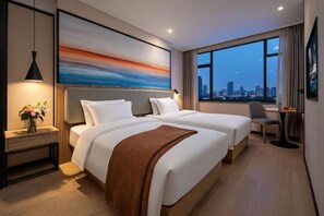 Habitació d'hotel amb dos llits, vista a la ciutat, una taula de treball i una cadira.