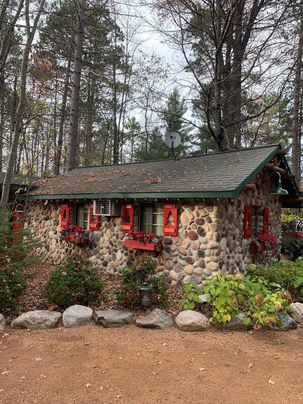 Una cabaña de piedra rústica con techo verde, rodeada por un bosque.