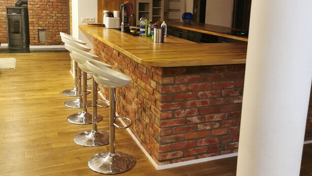 Une cuisine moderne avec un mur d’accent en briques, un comptoir de bar en bois et des tabourets de bar en acier inoxydable.