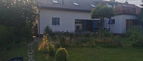 Una casa con techo de tejas, un jardín con sendero y un pequeño árbol.