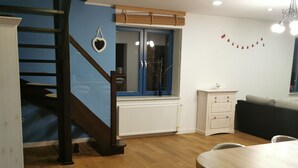 Une cuisine moderne avec un escalier en bois, une fenêtre avec des rideaux, un radiateur et un coin repas équipé d’un tabouret de bar.