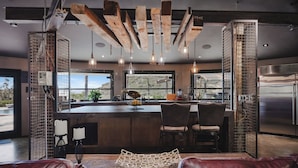 Une cuisine moderne dotée d’un îlot central, de tabourets de bar, de luminaires suspendus et d’un réfrigérateur en acier inoxydable.