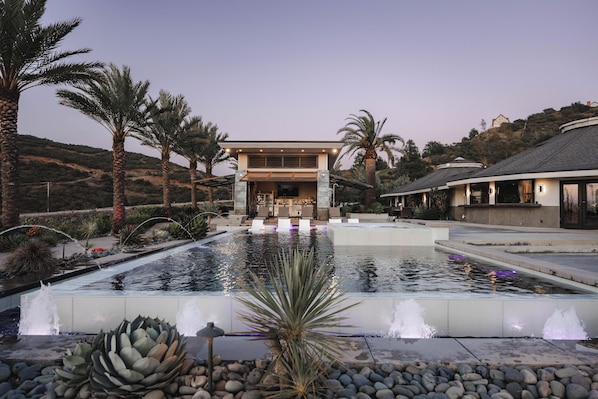 Un hotel moderno con piscina, palmeras y un paisaje montañoso.