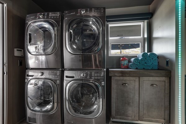 A laundry area with four stacked front-loading washing machines, a window with a view, and a cabinet with towels.