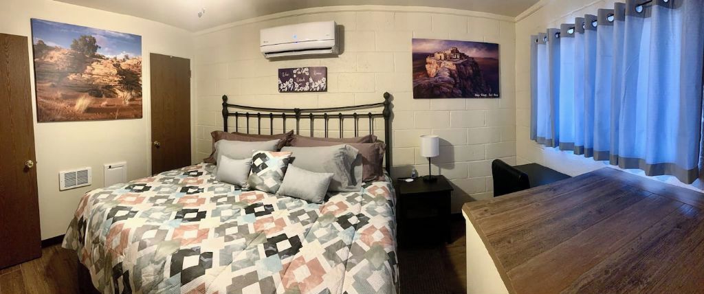 A bedroom with a bed, a nightstand, a wall-mounted air conditioner, and two framed pictures.