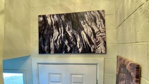 Un pasillo con una puerta blanca, un cuadro abstracto colgado en la pared y una escultura de madera.