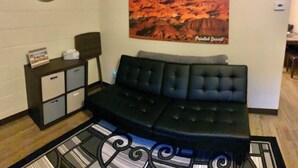 Una sala de estar con un sofá negro, un reloj, un cartel y un mueble bajo.