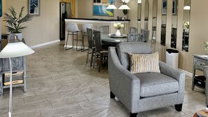 Una sala de estar moderna con un sillón gris, un comedor con mesa y sillas, y una cocina al fondo.
