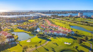 Vista aérea de un campo de golf con un club house, cuerpos de agua y edificios residenciales circundantes.