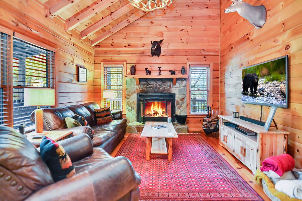 L’intérieur d’un chalet confortable, avec une cheminée, un canapé en cuir et un téléviseur.