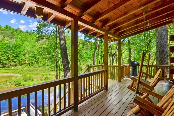 A wooden deck with a railing overlooking a forested area and a body of water.