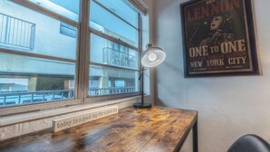 Ein Zimmer mit einem Holztisch, einem Fenster mit Blick auf Gebäude und einem Poster an der Wand.