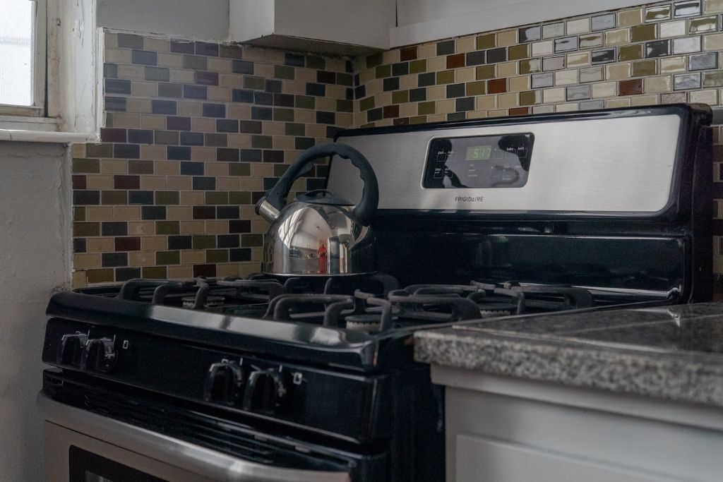 A kitchen with a black stove, a kettle, and a tiled backsplash.