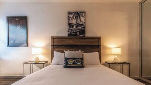 Ein Hotelzimmer mit einem großen Bett, zwei Nachttischlampen, einem gerahmten Bild an der Wand und einem Kopfkissen mit einem Logo.