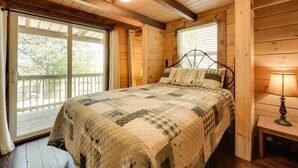 Ein Schlafzimmer einer Holzhütte mit einem Bett, einem Nachttisch, einer Lampe und großen Fenstern.