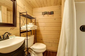 Un baño de cabaña de madera con un lavabo, un inodoro y un estante con toallas dobladas.