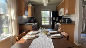 A dining area with a wooden table, chairs, and a striped table runner. There are two hanging pendant lights above the table. - McKinley House Prime - Patio, Pool and Garage (Amarillo)