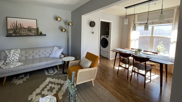 A modern living room with a grey sofa, a dining area with a wooden table and chairs, a floor lamp, and a view of the outside. - McKinley House Prime - Patio, Pool and Garage (Amarillo)