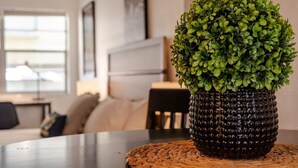 Ein Blumentopf auf einer gewebten Tischmatte auf einem Tisch in einem modern gestalteten Raum, mit einer Couch und einer Lampe.
