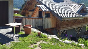 Eine Holzhütte mit geneigtem Dach, einem Schornstein und einer kleinen Veranda mit Tisch und Stühlen.