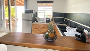 A compact kitchen with a microwave, toaster, and sink. A wooden table with a fruit bowl is in the foreground. - Villa Ti Ma-El, F2 quiet sea view Sainte-Anne   (sainte anne)